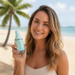 woman holiding a bottle of surfchique spray perfume with a beach and palm tree in the background